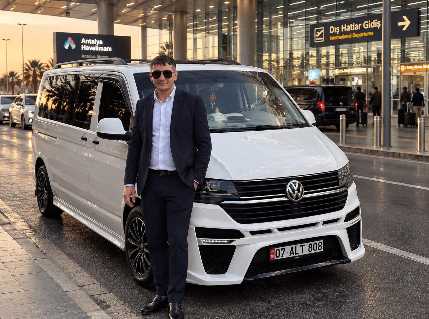 A man in a dark suit standing beside a white van outside Antalya Airport.